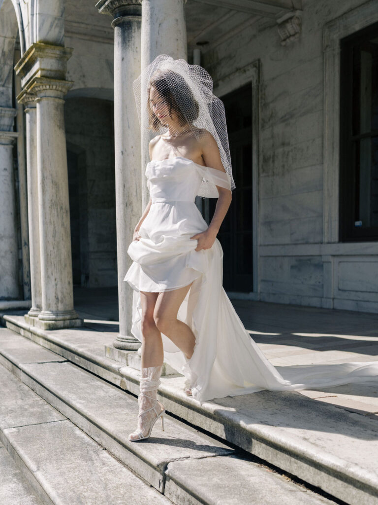 bride lifting skirt of wedding dress walking down mansion stairs